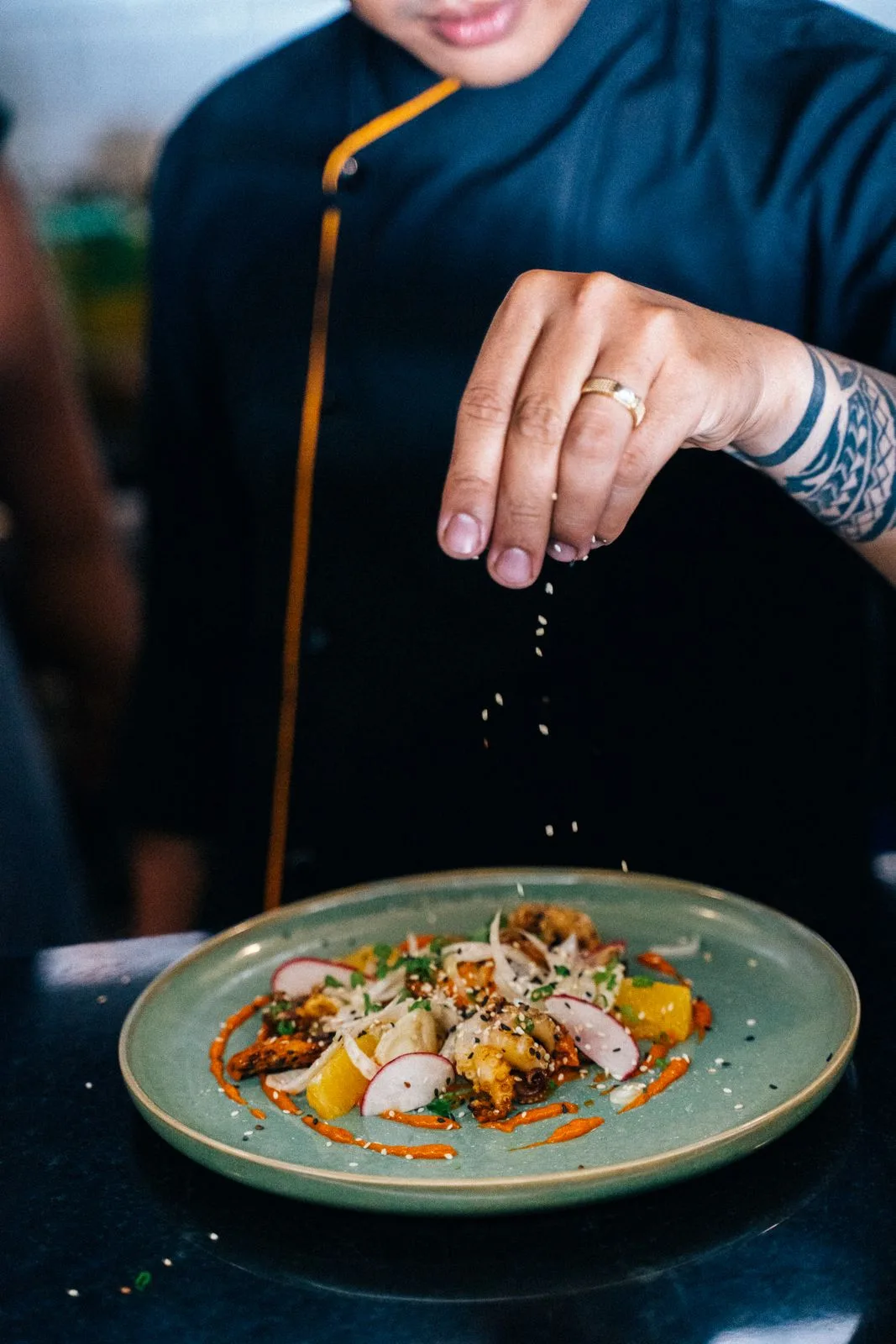 Les mains du chef saupoudrent des graines de sésame sur un plat dressé, dans une cuisine sombre